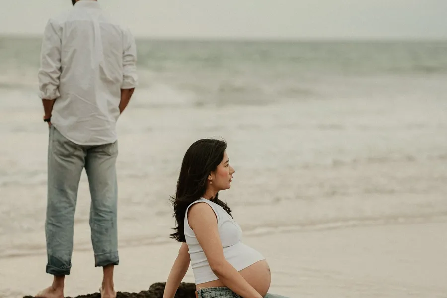 An expecting couple posing for maternity photos on the beach