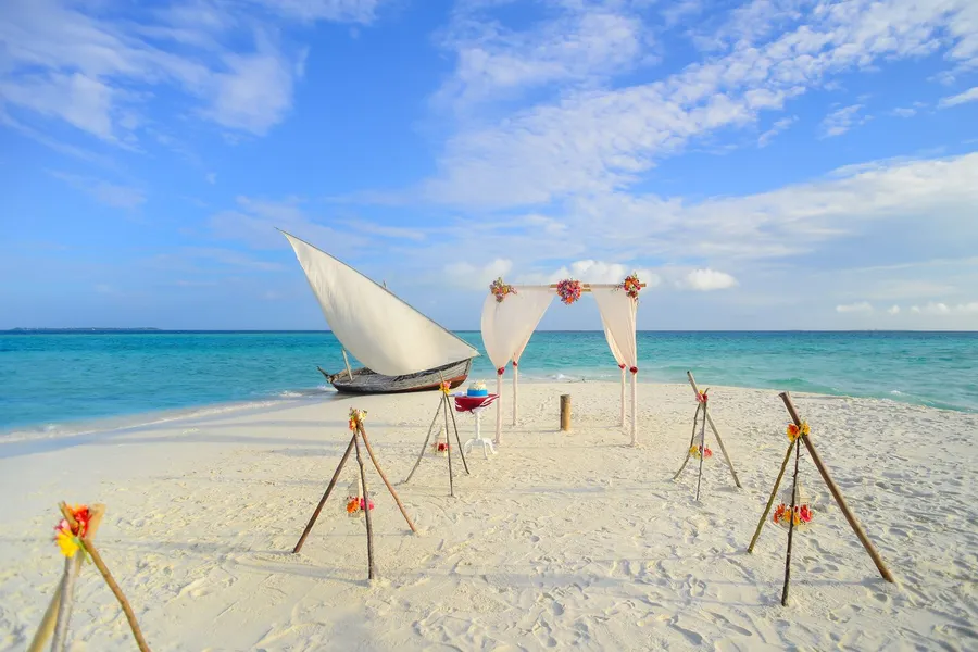 A decorated beach wedding aisle leading to an arch by the water
